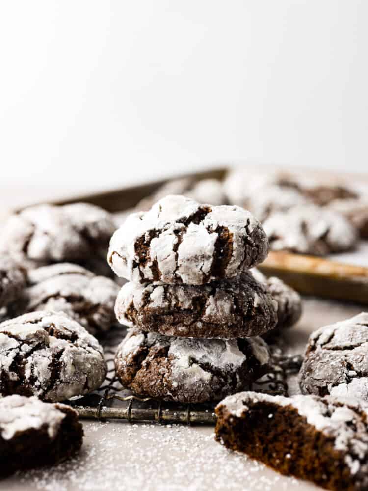 Side view of chocolate crinkle; cookies stacked on top of each other. The cookies are on a cooling rack and surrounded by additional cookies.