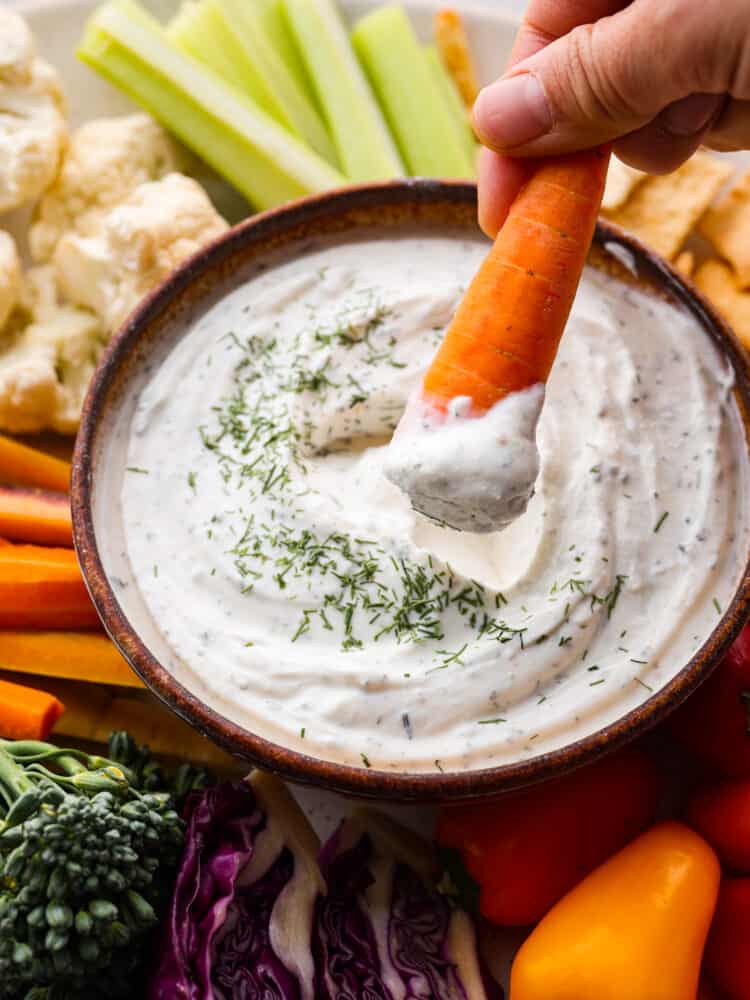 A carrot being dipped into the Greek yogurt dip.