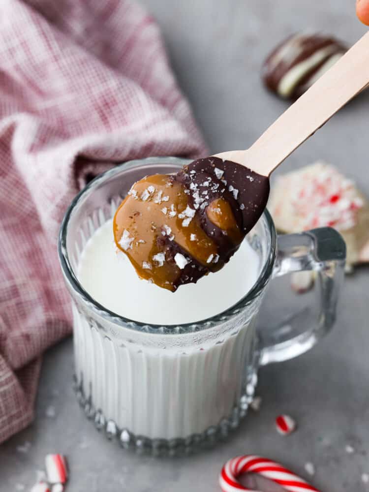 A hot chocolate spoon hovering above milk in a glass mug.