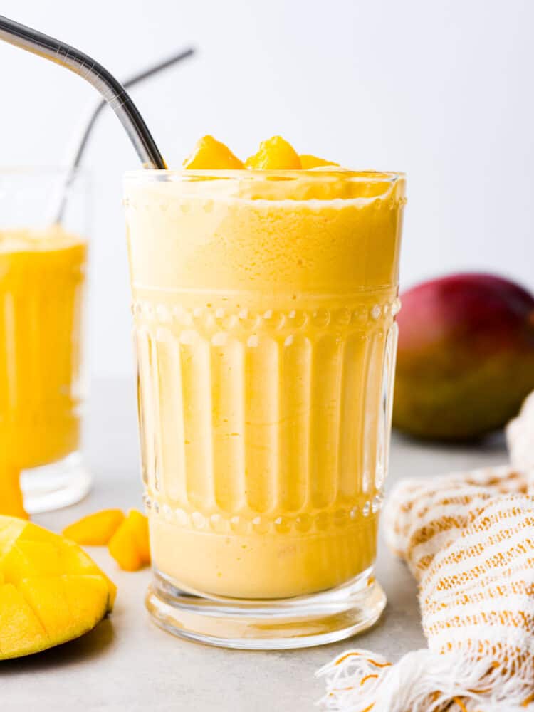 A mango lassi in a glass cup with a metal straw.
