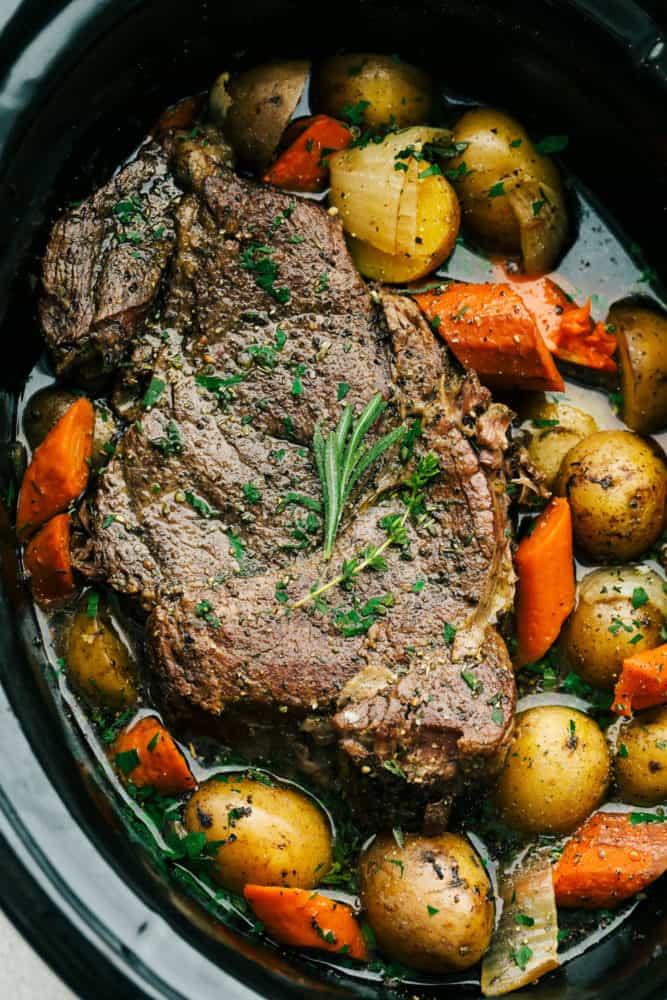 Top-down view of pot roast and vegetables in a slow cooker.