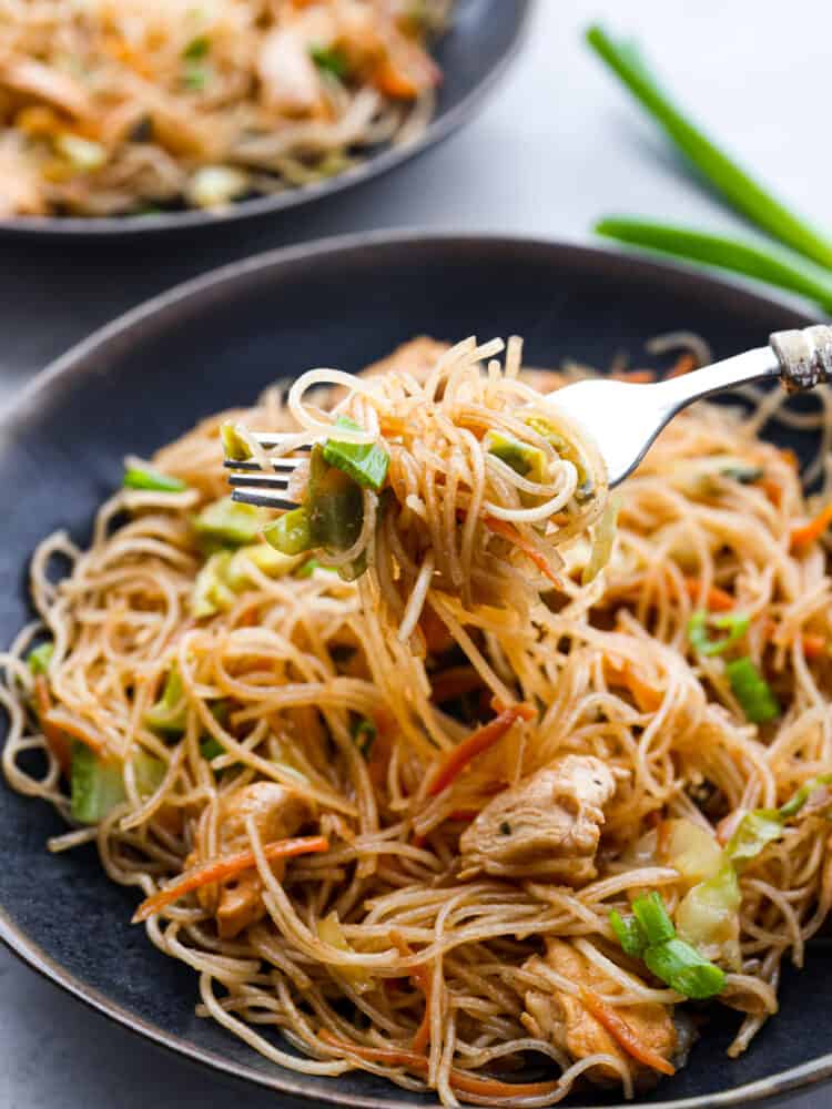 Close up view of pancit noodles lifting out of a black bowl with a fork.