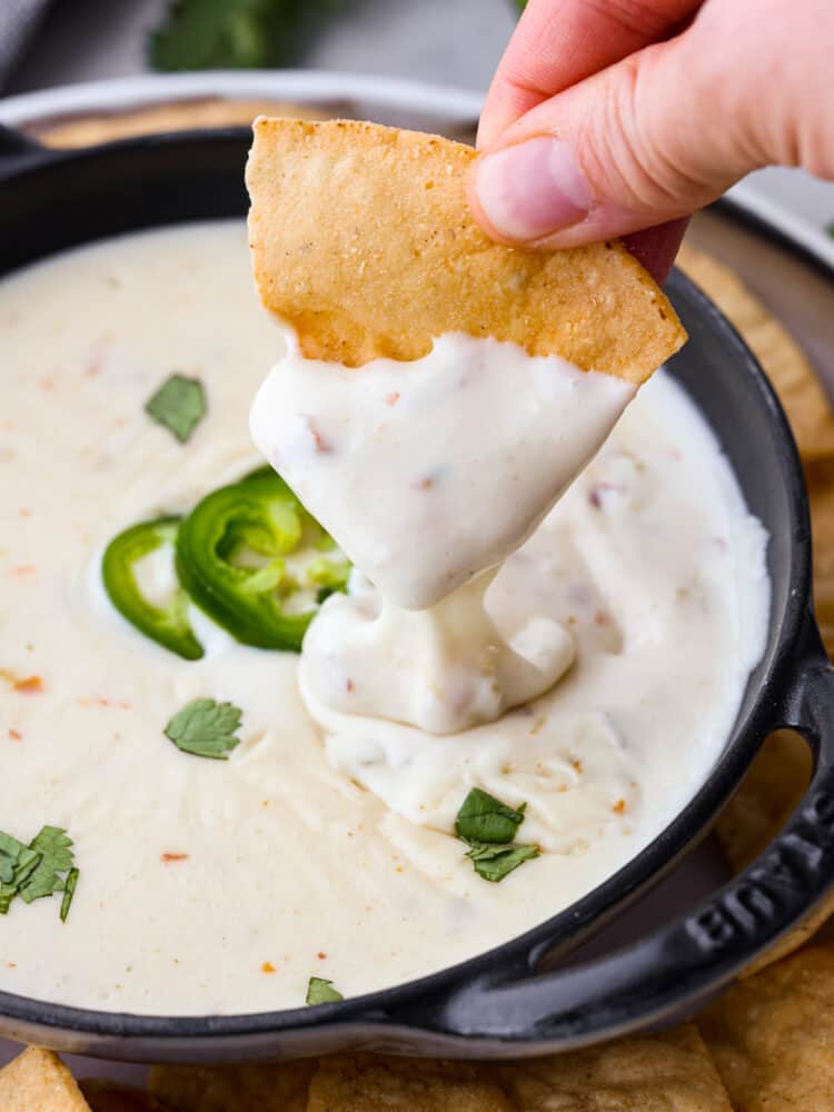 A tortilla chip being dipped into queso blanco.