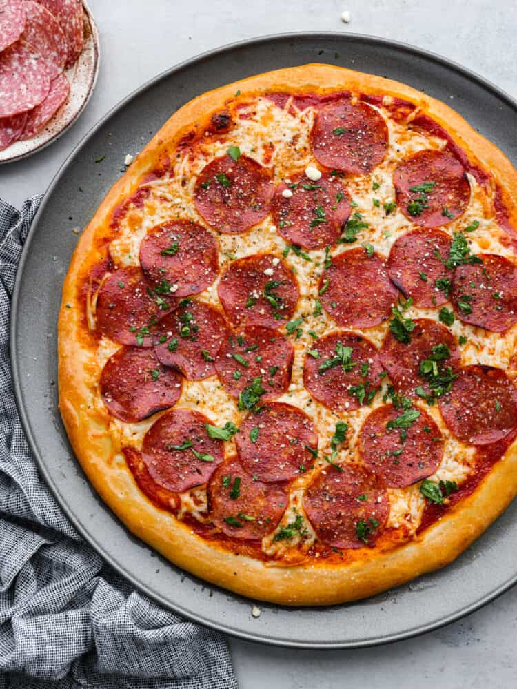 A whole salami pizza on a large plate.