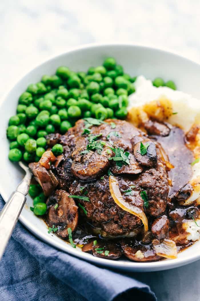 Skillet Salisbury Steak on a white plate with green peas and mashed potatoes.