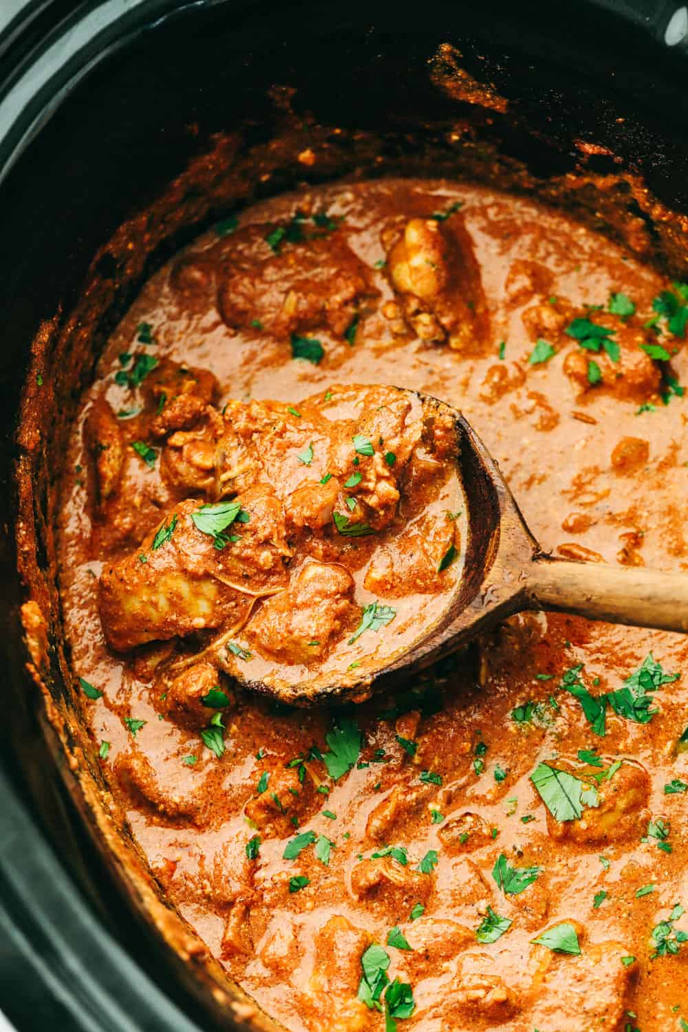 Chicken tikka masala in a slow cooker with a wooden spoon.
