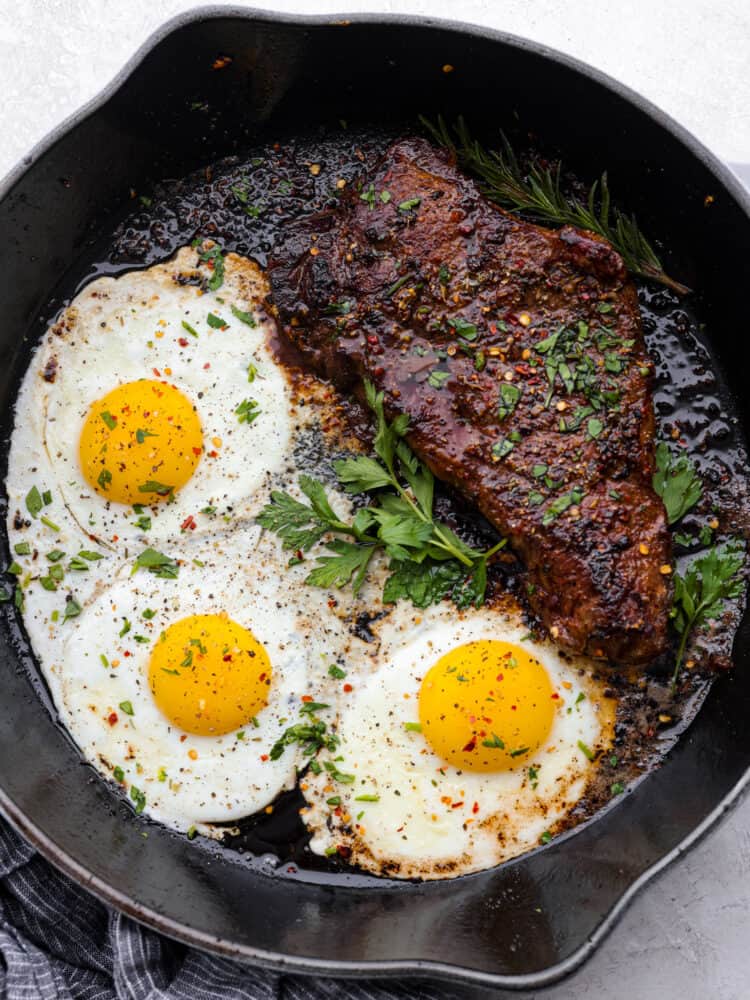 Top view of steak and eggs in a black skillet and garnished with fresh parsley.