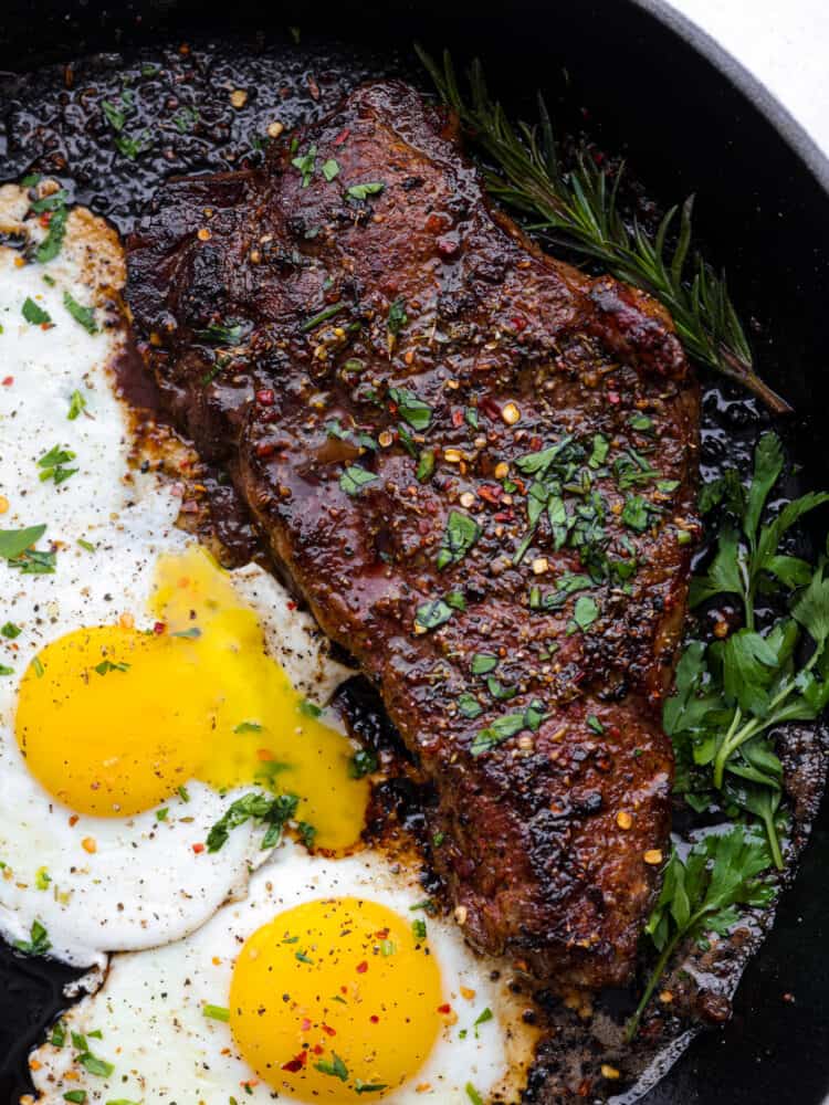 Close view of steak and eggs in a black skillet and garnished with fresh parsley.