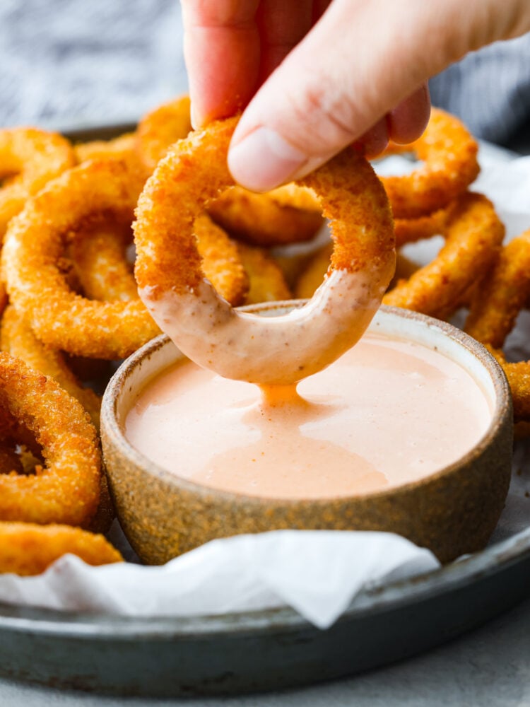 A hand dipping them in a bowl of fry sauce.