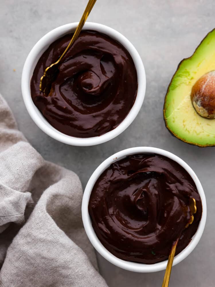 Chocolate avocado pudding in two bowls with a fresh avocado cut open.