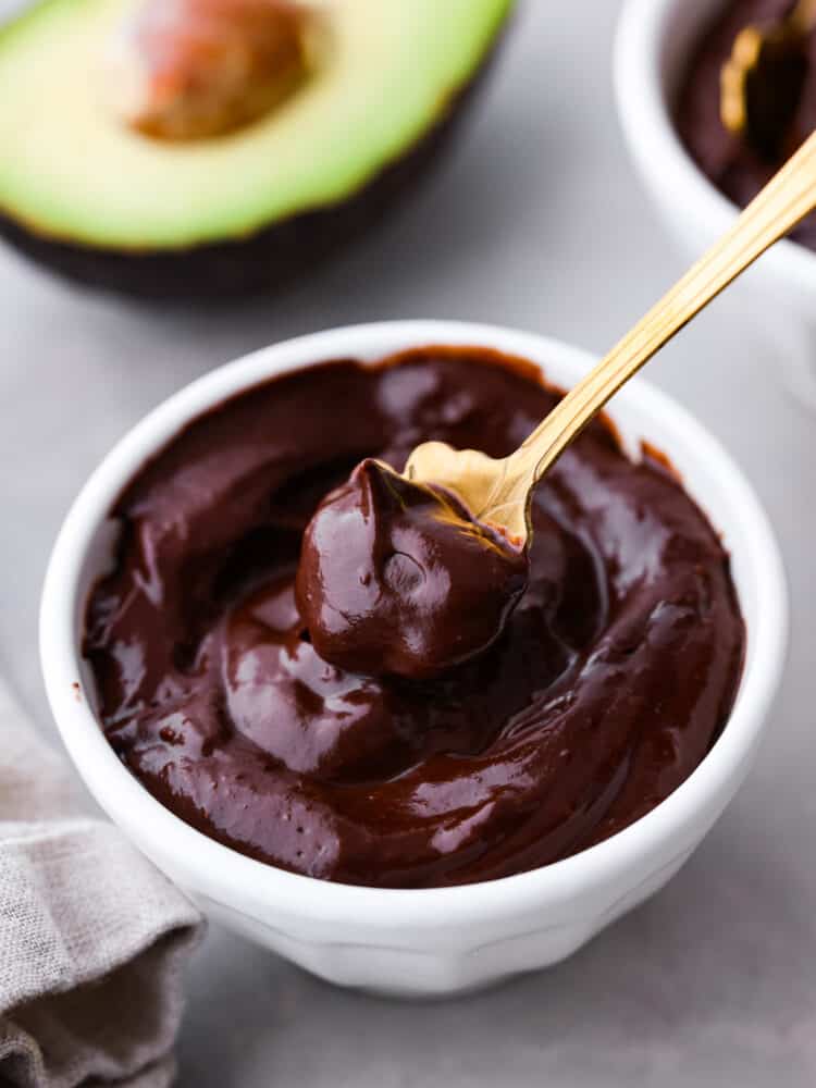 Chocolate avocado pudding in a white bowl with a gold spoon taking a spoonful.