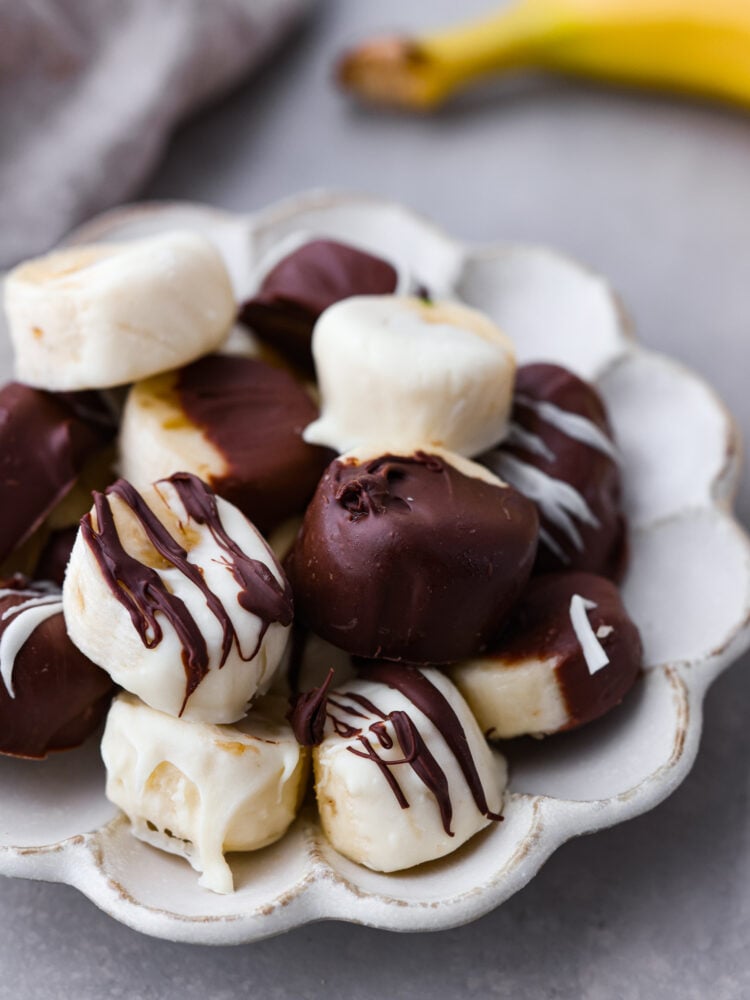 Chocolate dipped bananas served on a white scalloped dish.