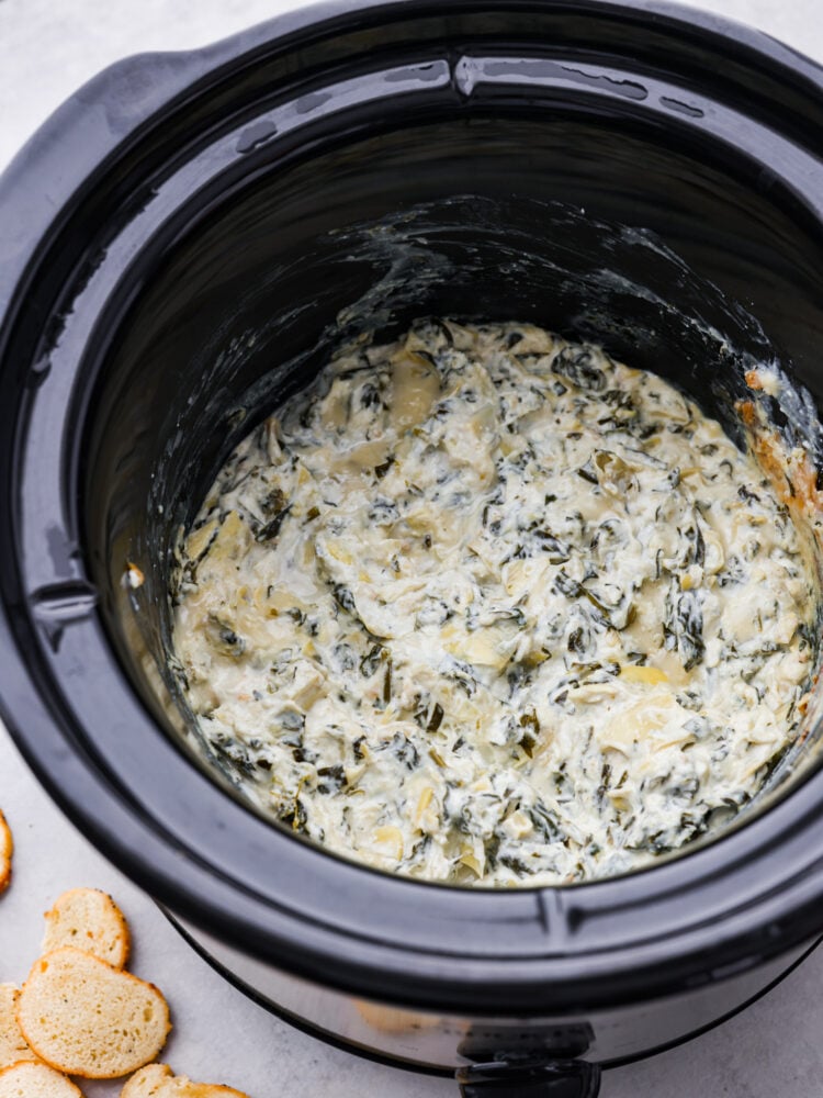 Cooked spinach artichoke dip in the bottom of a crockpot.