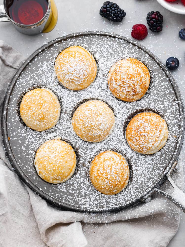 An overhead view of the ebelskivers cooked in their pan with powdered sugar on top.