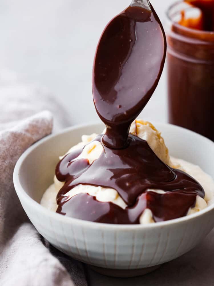 A spoon drizzling hot fudge over a bowl of ice cream.
