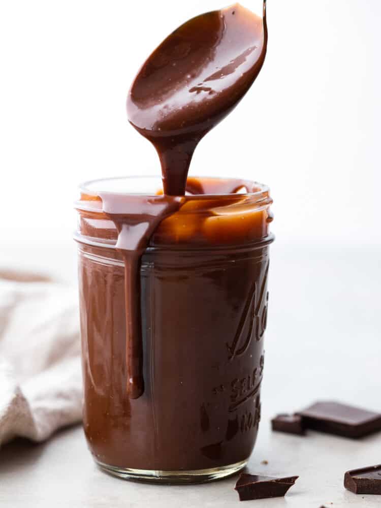 A spoon pulling out of a jar of hot fudge.
