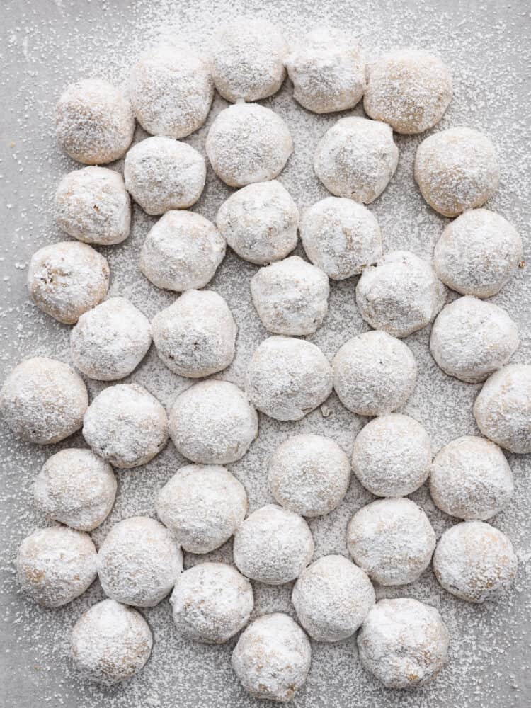 Mexican wedding cookies on a counter top covered in powdered sugar.