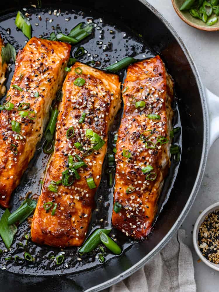 Miso glazed salmon in a pan with sesame seeds and green onions on top.