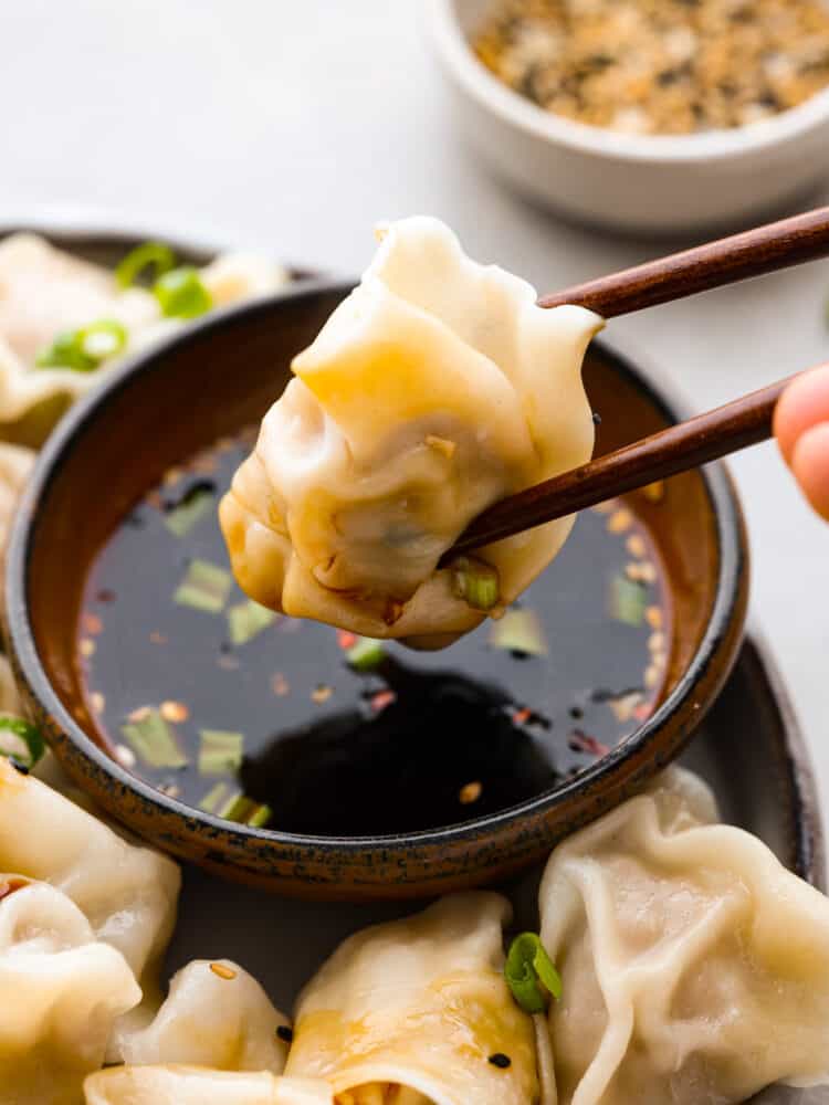 A pork wonton being dipped in sauce with chopsticks.