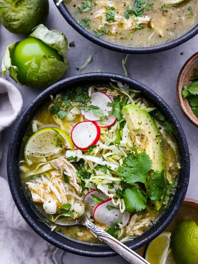 Pozole verde in a black bowl with fresh ingredients around it.