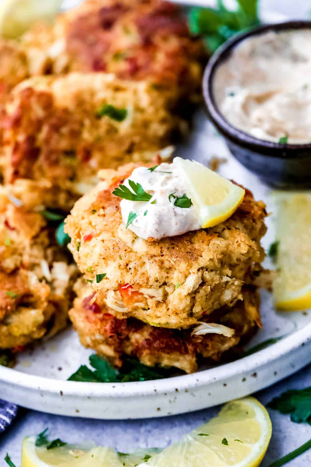 Crab cakes on a white plate, topped with tartar sauce.