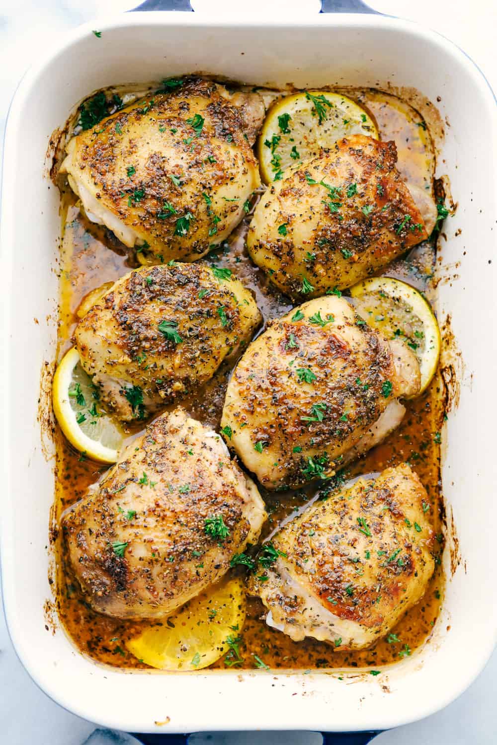 Baked chicken thighs in a baking pan with lemon slices. 