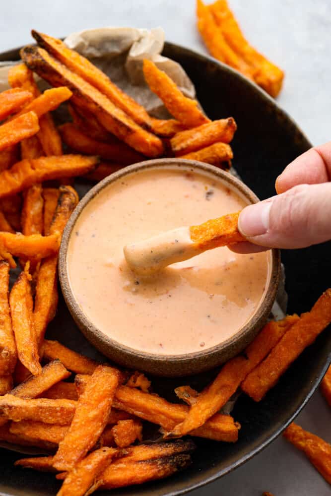 A hand dipping a french fry into the boom boom sauce.