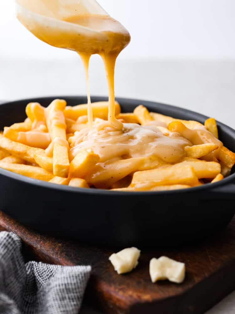 French fries in a dish with gravy being poured over them.