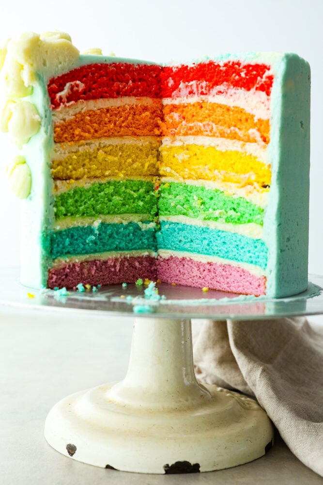 A whole rainbow cake with a slice cut out of it.