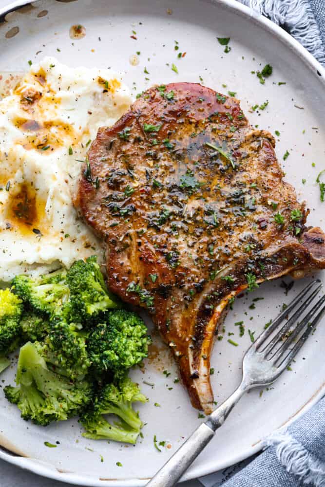 A cast iron skillet pork chop on a plate with mashed potatoes and broccoli.