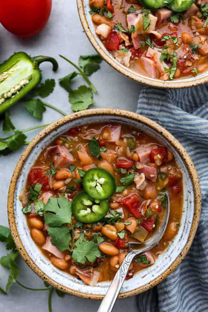 Mexican Charro Beans, also known as Frijoles Charros, are loaded to the brim with flavor! Pinto beans are cooked in a chicken broth seasoned with warm and inviting spices. Throw in some bacon, tomato, onions, ham, and jalapeños for the perfect blend of bold flavors. Charro beans in a bowl with a spoon.