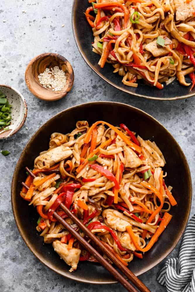Chicken lo mein in a black bowl with other bowls around it.