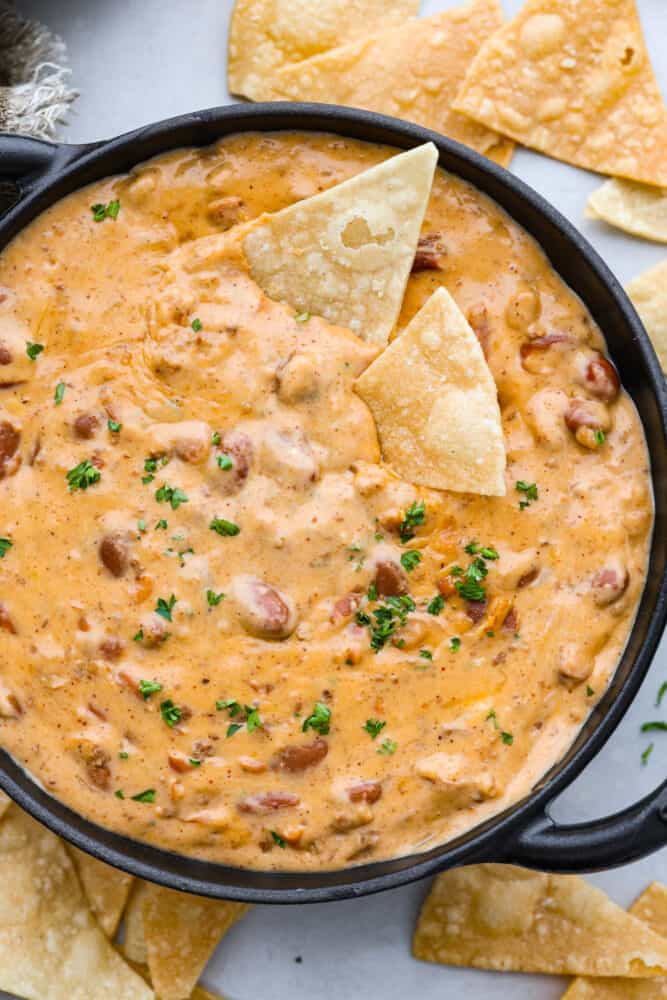 Top-down view of chili cheese dip served with chips in a black bowl.