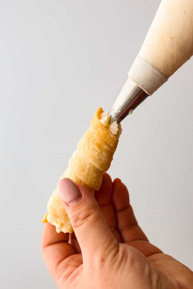 A cream horn cookie shell being piped with filling.