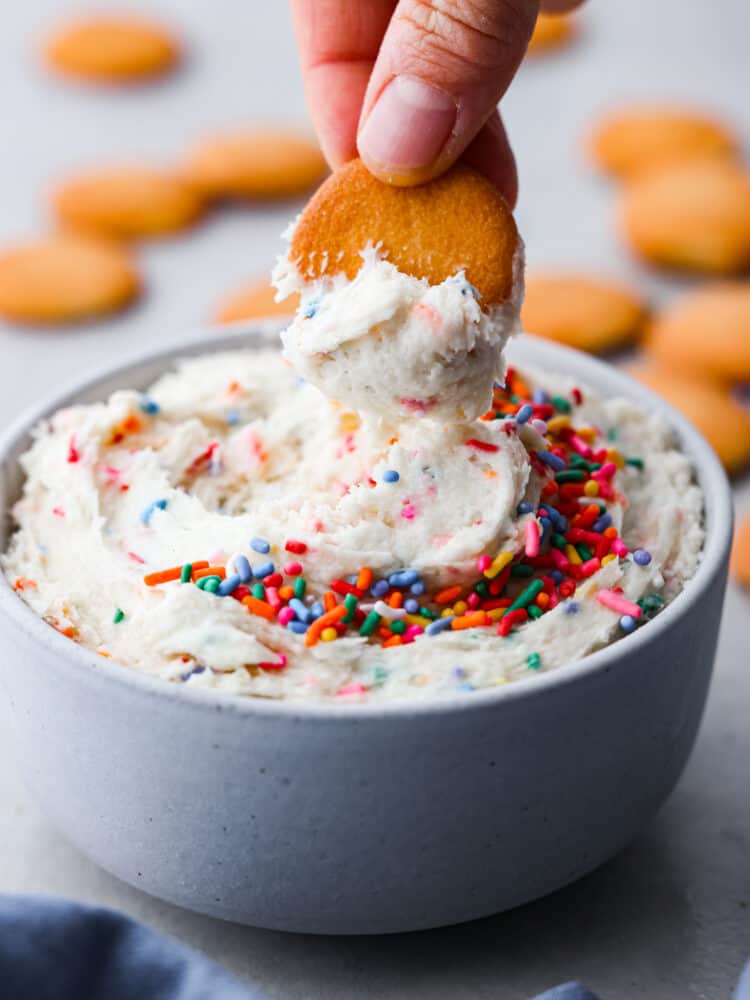 A hand dipping a vanilla wafer cookie into dunkaroo dip.
