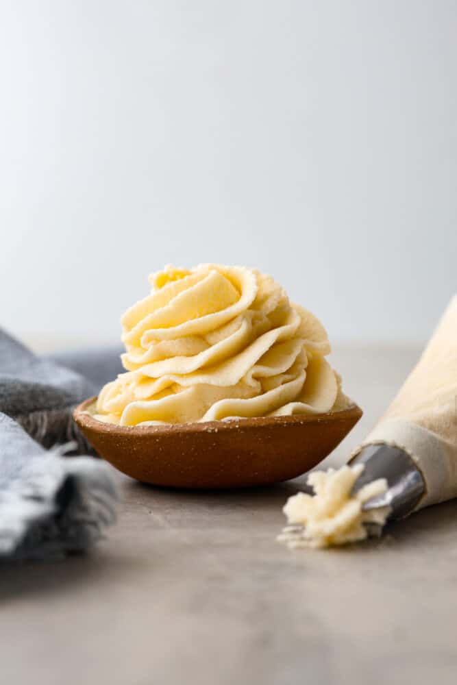 Ermine frosting in a little bowl with a piping bag next to it.
