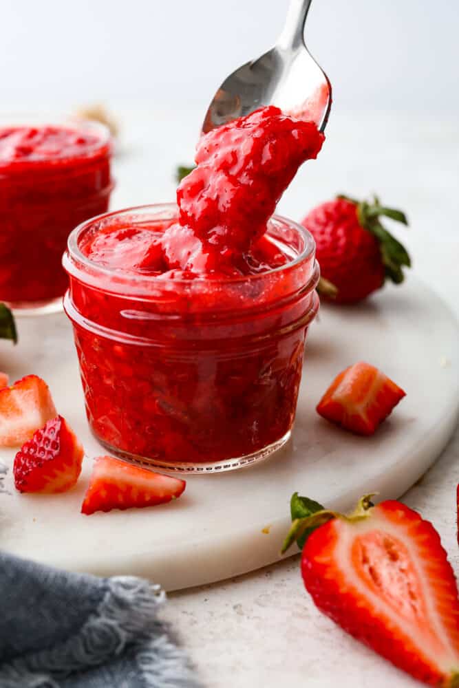 Strawberry sauce in a jar with a spoon taking some out.