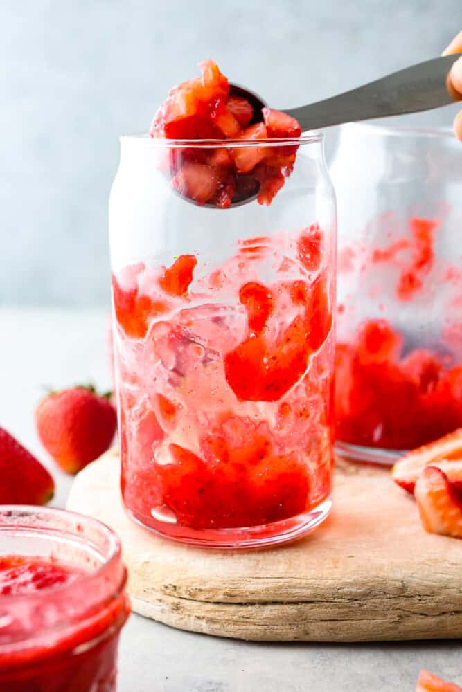 Adding chopped strawberries to a glass cup.