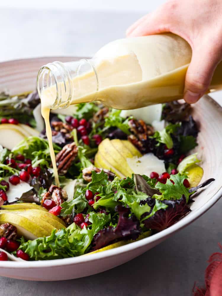 A bottle of champagne vinaigrette being poured onto the salad. 