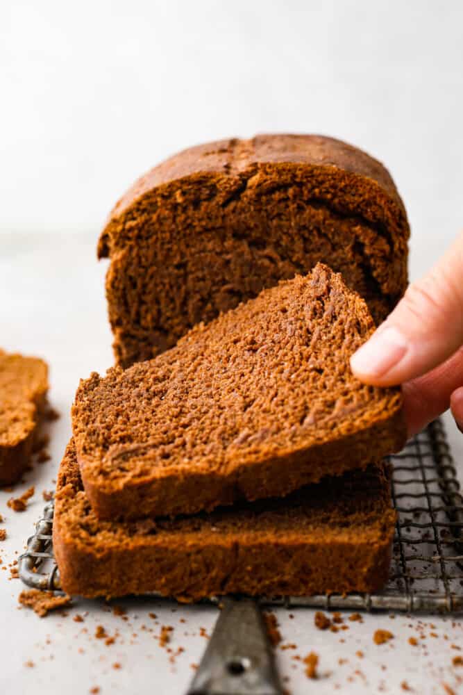 A hand picking up a slice of pumpernickel bread.
