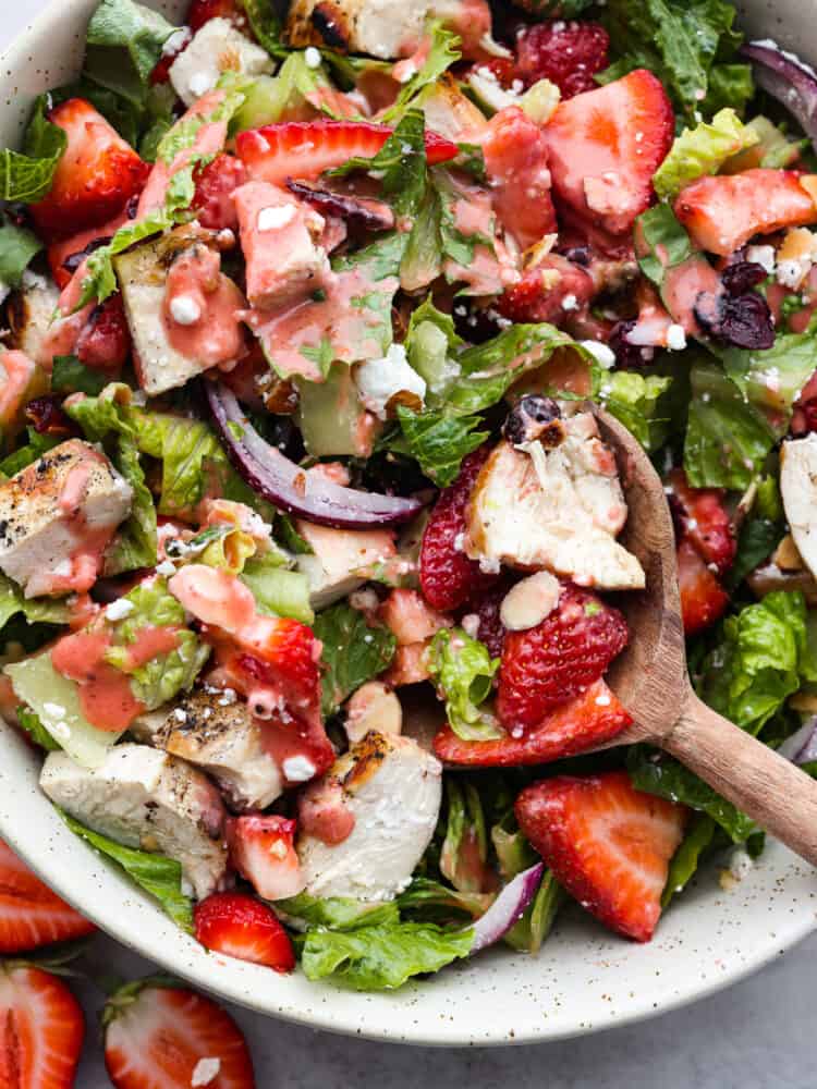 A close up of strawberry chicken salad with a wooden spoon in the bowl. 