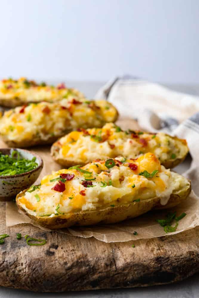Twice-baked potatoes topped with bacon, cheese, and green onions, served on a wooden board.