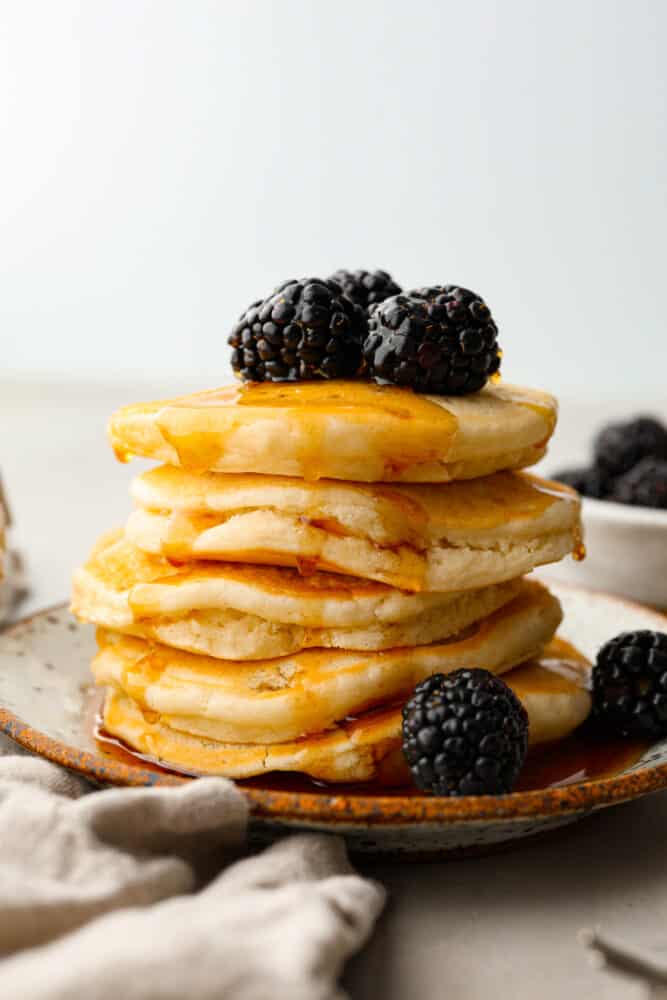 A stack of vegan pancakes topped with blackberries and maple syrup.