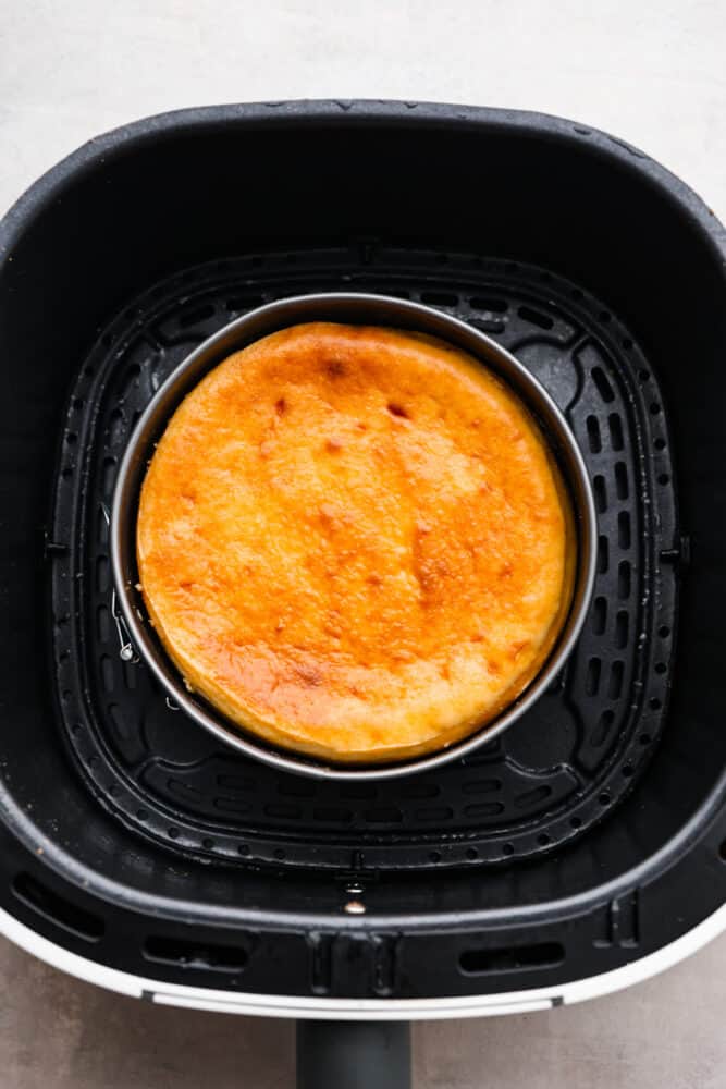 A cooked cheesecake in the bottom of an air fryer basket.