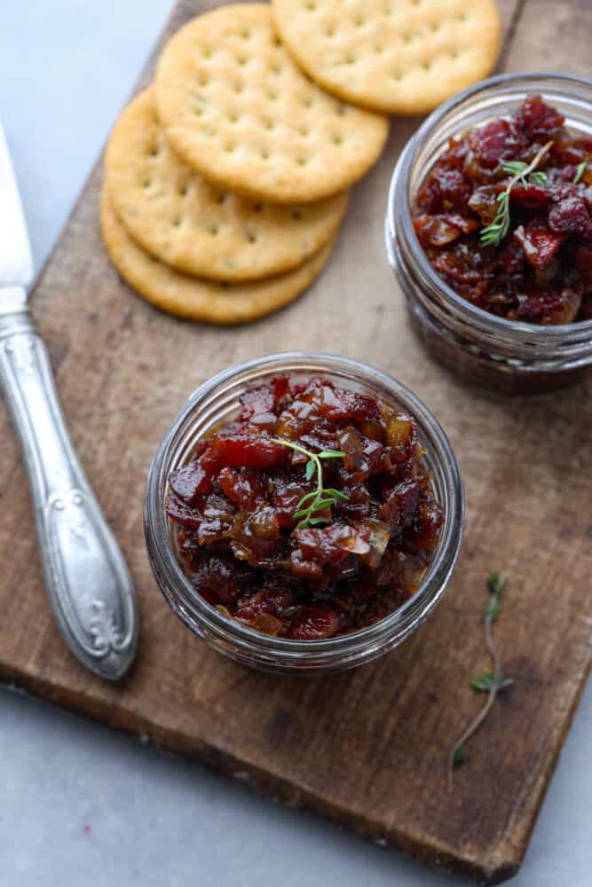 Top-down view of bacon jam in a glass jar on a wooden board served with crackers.