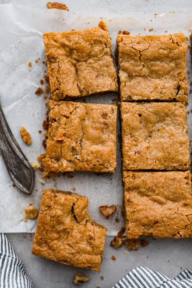 An overhead view of brown butter blondies on parchment with one piece with a bite taken out of it.