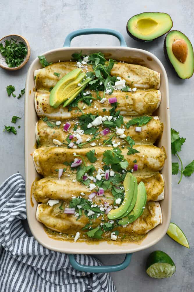 A top view of chicken enchiladas with an avocado cream sauce in a casserole dish. 
