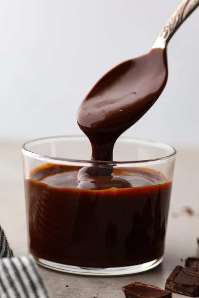 Chocolate ganache in a glass container with a spoon taking a scoop out.