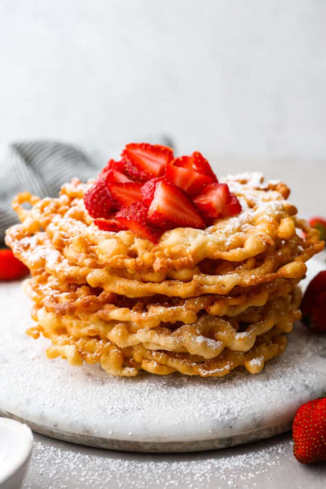 Funnel cakes stacked on top of each other topped with strawberries and powdered sugar.