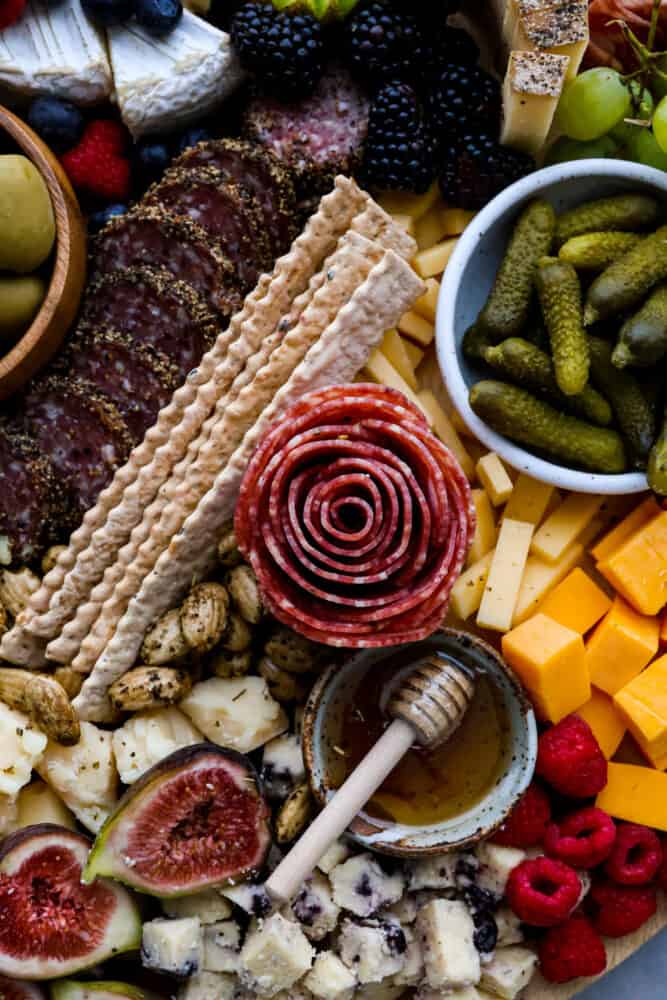A salame rose surrounded by things like pickles, cubed cheese, honey, and crackers.
